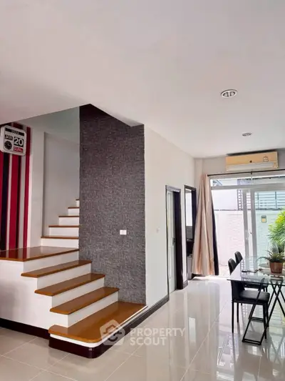 Modern interior with sleek staircase and dining area, featuring stylish decor and ample natural light.