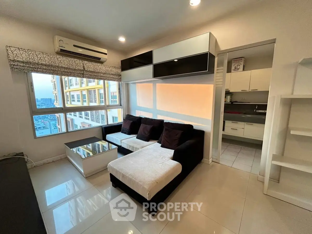 Modern living room with sleek furniture and city view, adjacent to a compact kitchen.