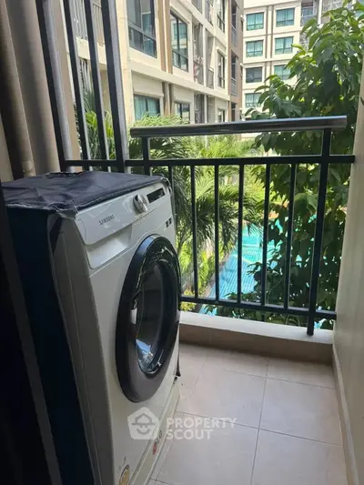 Charming balcony with washing machine overlooking lush greenery and pool view in modern apartment complex.