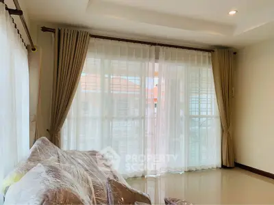 Spacious living room with large windows and elegant curtains, perfect for natural light and comfort.