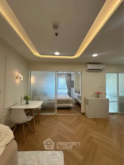 Modern living room with elegant lighting and cozy dining area, featuring a view into a stylish bedroom.