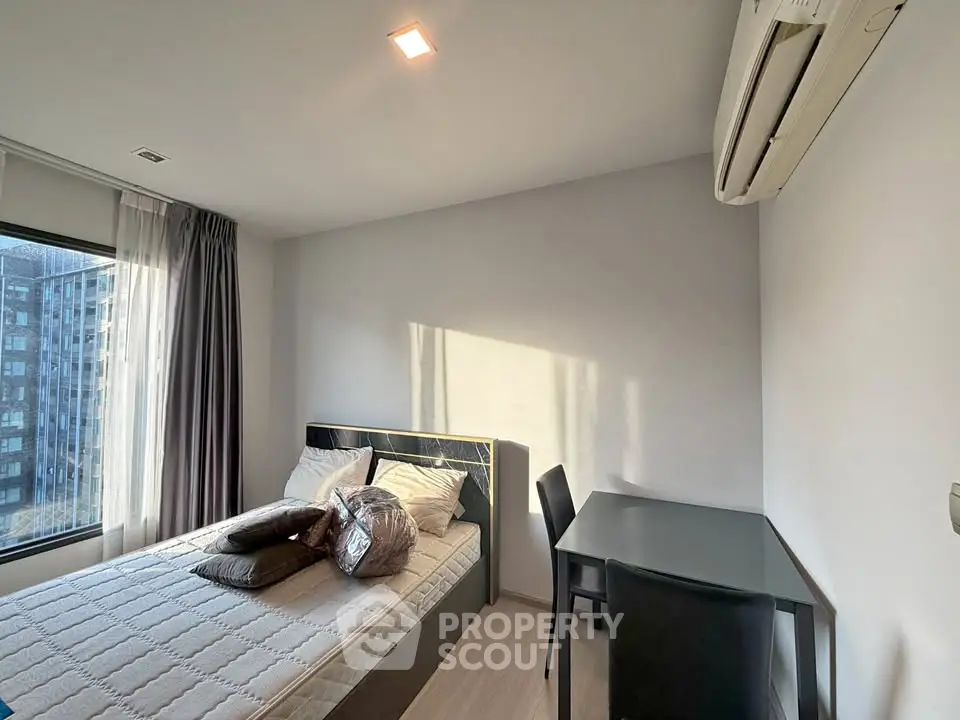 Modern bedroom with natural light, featuring a cozy bed and workspace, ideal for urban living.