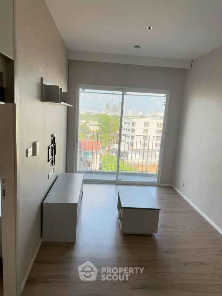 Modern living room with large window offering city view, featuring sleek furniture and wooden flooring.