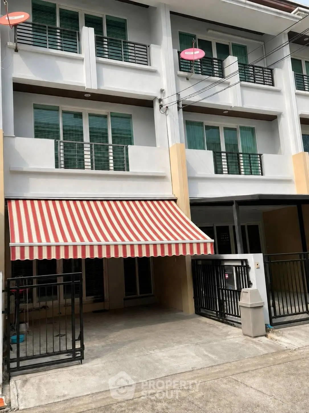 Modern townhouse exterior with striped awning and gated parking area, ideal for urban living.