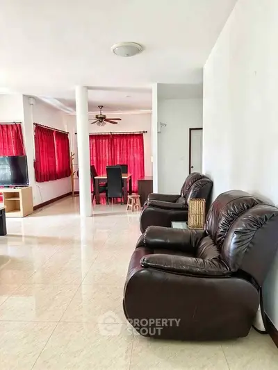 Spacious living room with leather sofas and dining area, featuring elegant red curtains and tiled flooring.