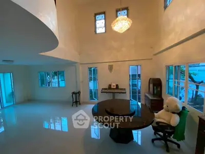 Spacious living room with high ceilings and elegant chandelier, featuring a piano and plush teddy bear for a cozy touch.