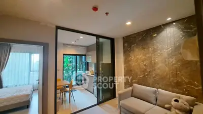 Modern apartment with open kitchen and cozy living area, featuring elegant marble wall and natural light.
