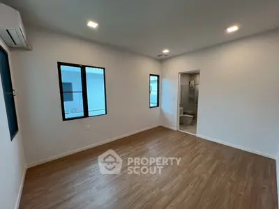 Spacious empty room with wooden flooring and modern lighting, featuring an ensuite bathroom.