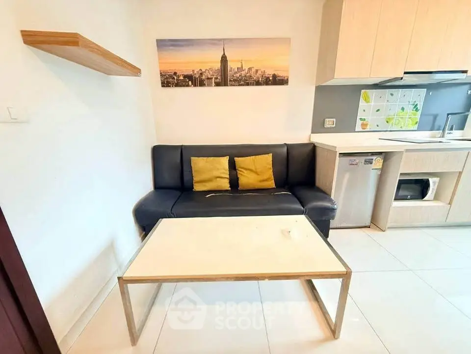 Modern living room with sleek black sofa, stylish wall art, and compact kitchen area.