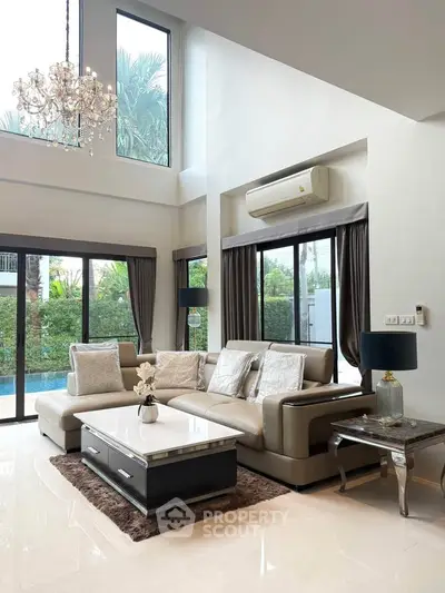 Luxurious living room with high ceilings, elegant chandelier, and pool view.