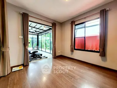 Spacious room with wooden flooring and large windows overlooking a garden, perfect for home gym setup.