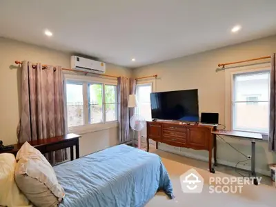 Cozy bedroom with modern decor, featuring a large TV and ample natural light from multiple windows.