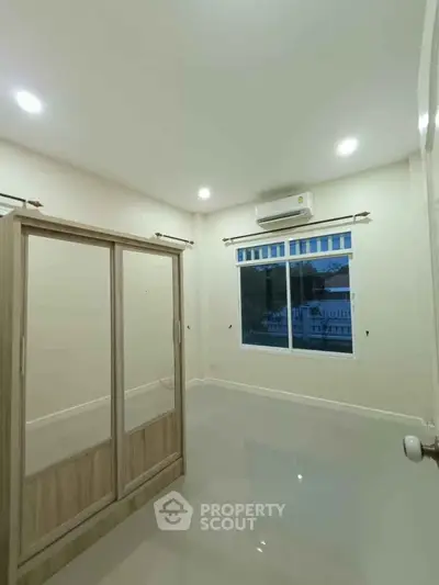 Spacious bedroom with large window and modern wardrobe in a serene setting.