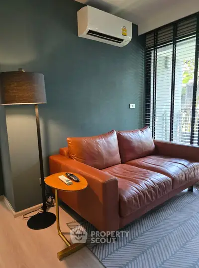 Modern living room with leather sofa and floor lamp, featuring air conditioning and large windows.
