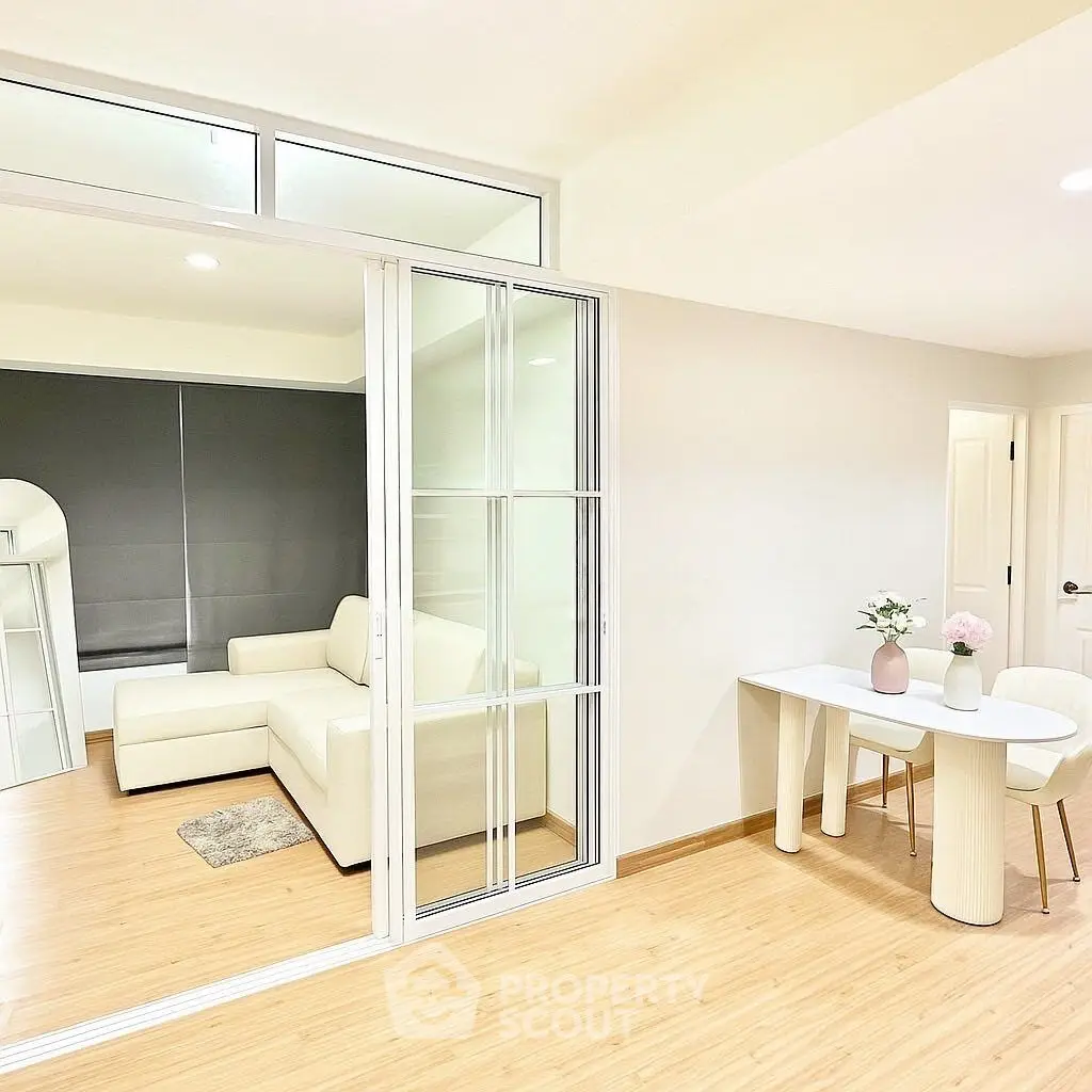 Modern living room with sliding glass doors and cozy dining area, featuring minimalist decor and light wood flooring.