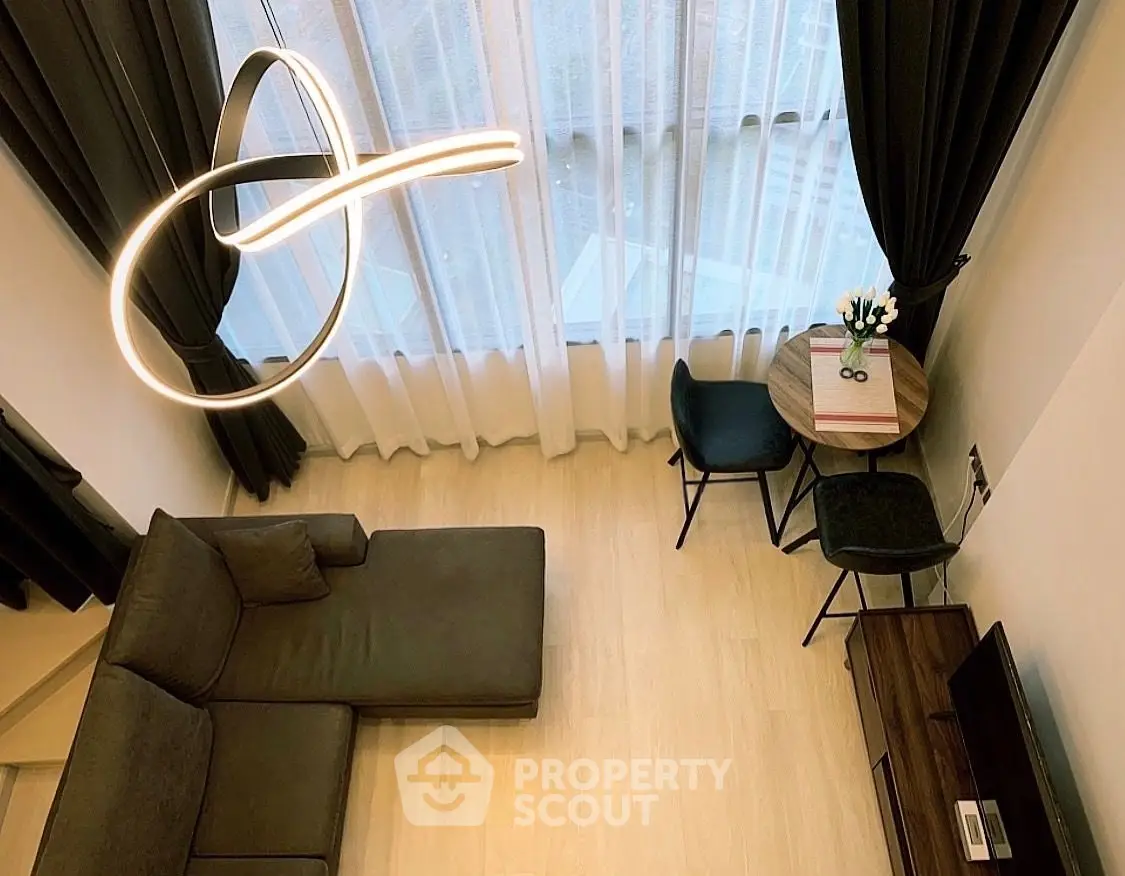 Modern living room with high ceiling, stylish lighting, and cozy seating area, perfect for urban living.