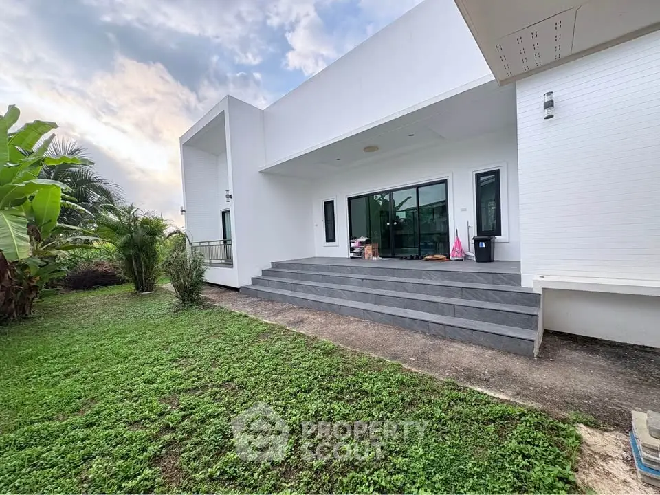 Modern white house with lush green garden and spacious patio