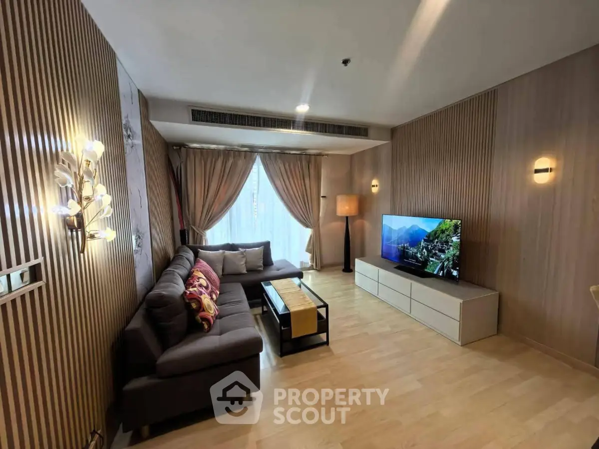 Modern living room with stylish decor and large TV, featuring cozy seating and elegant lighting.