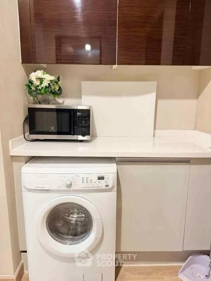 Modern kitchen with washing machine and microwave, sleek cabinets, and elegant decor.
