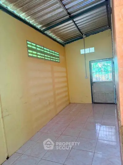 Spacious tiled room with metal roof and natural light, ideal for storage or utility use.