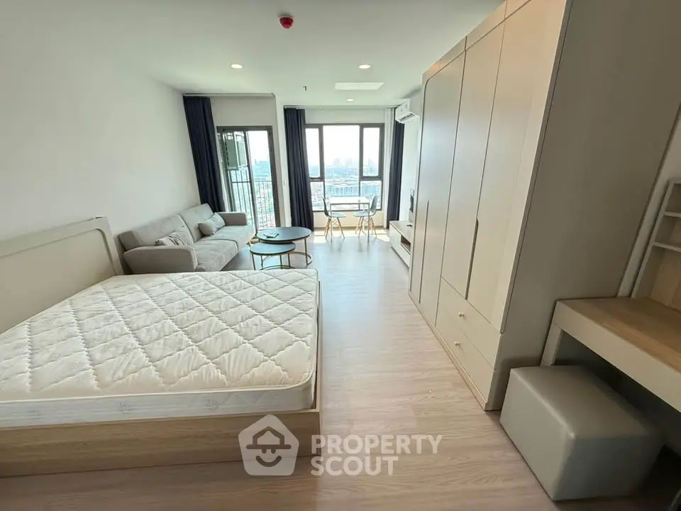 Modern studio apartment with open layout, featuring a cozy living area and large windows with city views.
