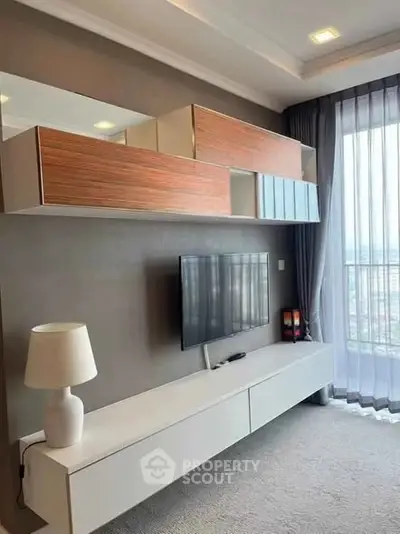 Modern living room with sleek TV unit and large window offering city views.