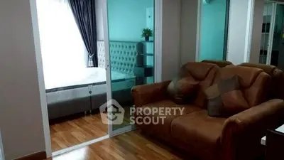 Cozy living room with brown leather sofa and view into a modern bedroom through glass doors.