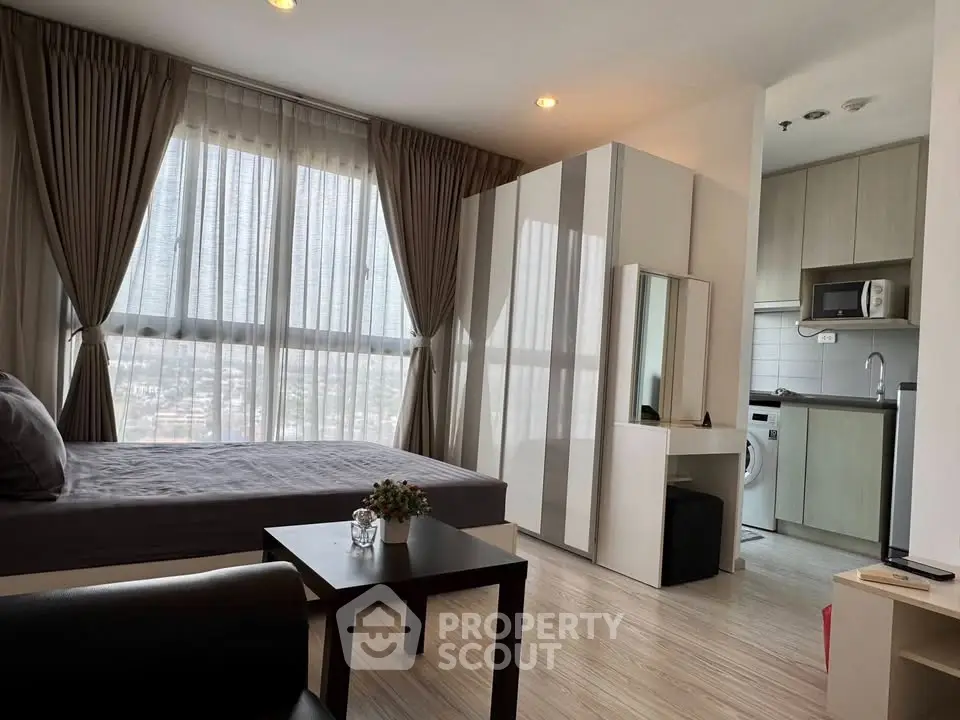 Modern studio apartment with large windows and compact kitchen in urban setting.