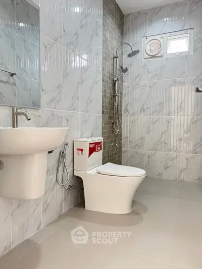 Modern bathroom with sleek fixtures and marble tiles, featuring a shower and toilet.