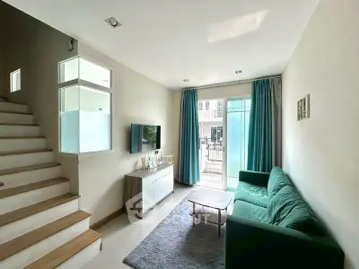 Modern living room with green sofa, TV, and natural light from large windows.