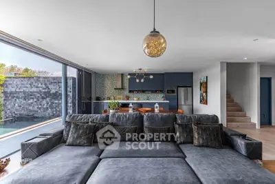 Luxurious open-plan living room with modern kitchen and pool view, featuring elegant decor and spacious seating.