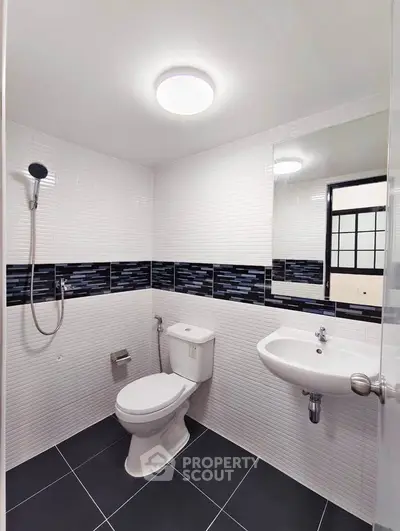 Modern bathroom with sleek black and white tiles, featuring a shower, toilet, and sink.