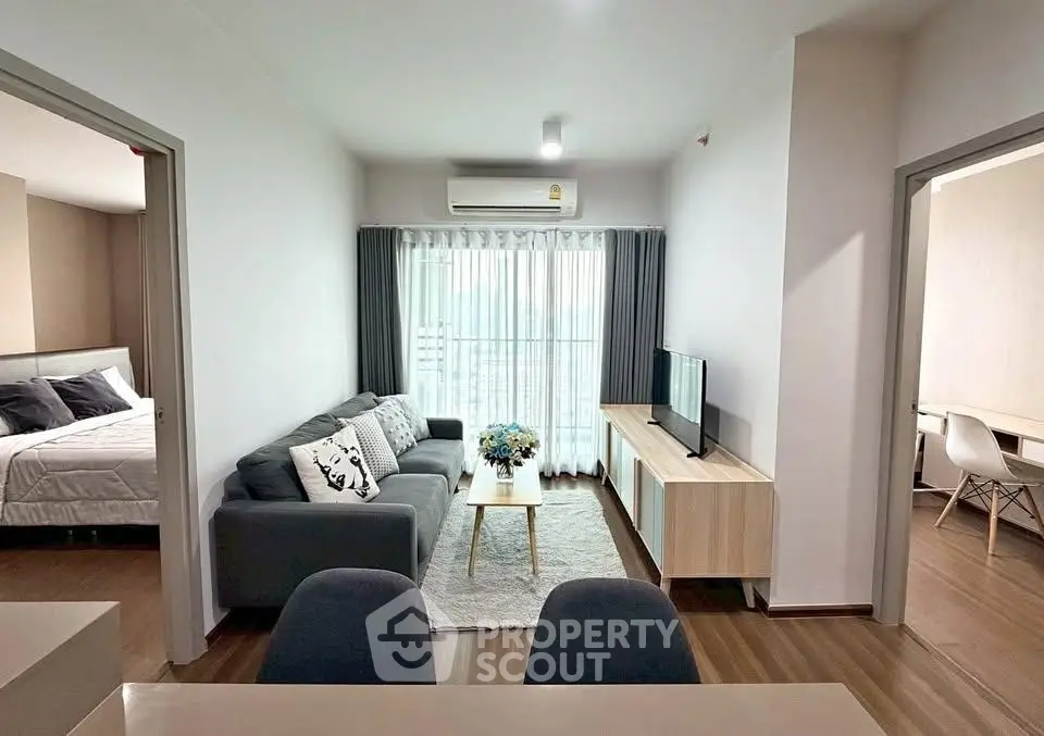 Modern living room with cozy sofa, TV, and natural light, adjacent to bedroom and study area.
