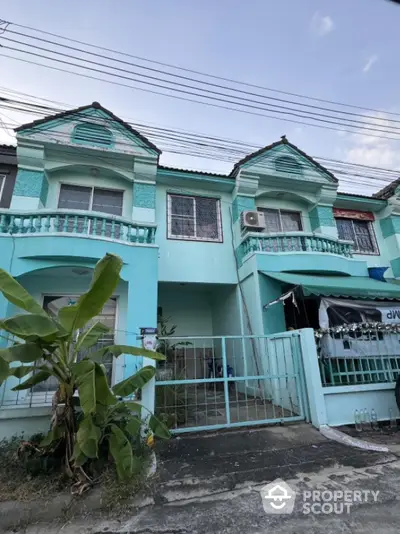 Charming turquoise townhouse with balcony and gated entrance in a serene neighborhood.