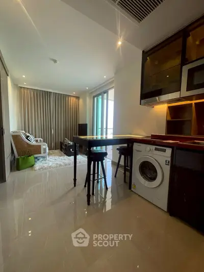 Modern open-plan living room with kitchen and washing machine, featuring sleek design and natural light.