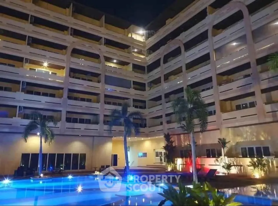 Luxurious apartment building with illuminated pool and palm trees at night.
