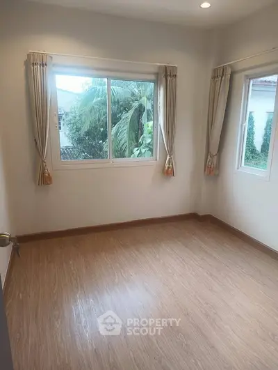 Bright empty room with large windows and wooden flooring, ideal for customization.