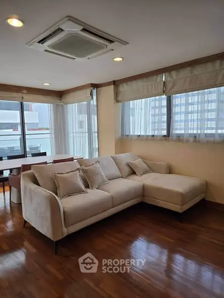 Spacious living room with modern L-shaped sofa and large windows offering city views.