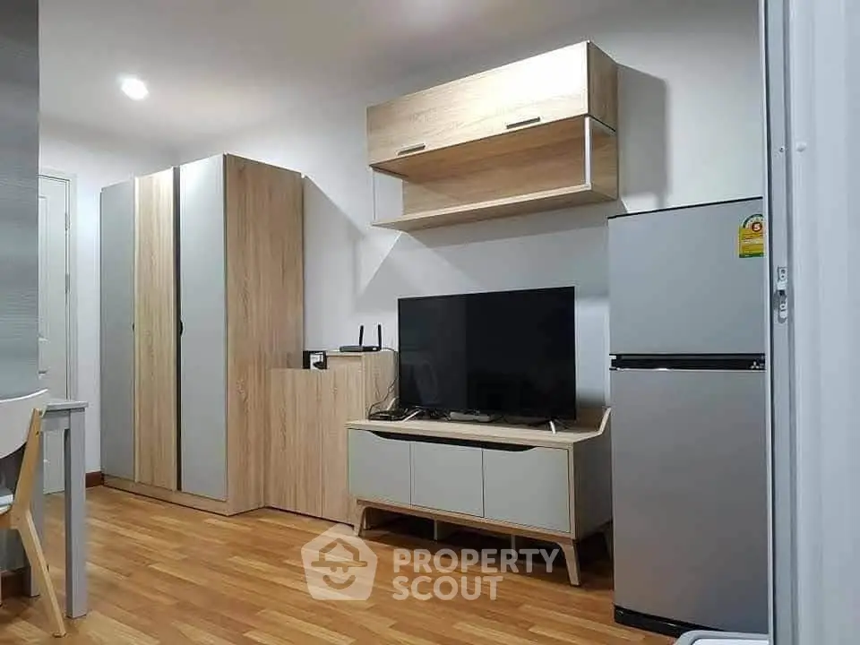 Modern living room with sleek furniture and appliances, featuring a TV and fridge on wooden flooring.