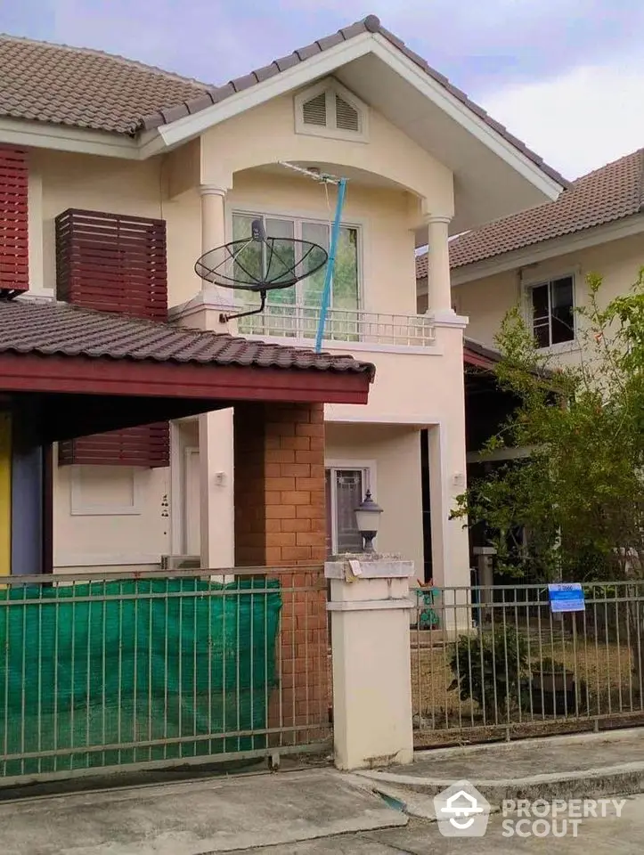 Charming two-story family home with a spacious balcony and red tile roofing, nestled in a serene neighborhood with lush greenery.