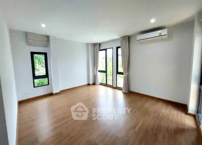 Spacious empty room with wooden flooring and large windows, ideal for customization.