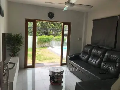 Modern living room with leather sofa and garden view through glass doors.