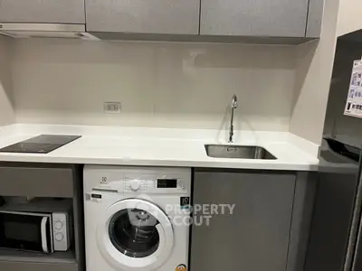 Modern kitchen with washing machine, microwave, and sleek cabinetry.