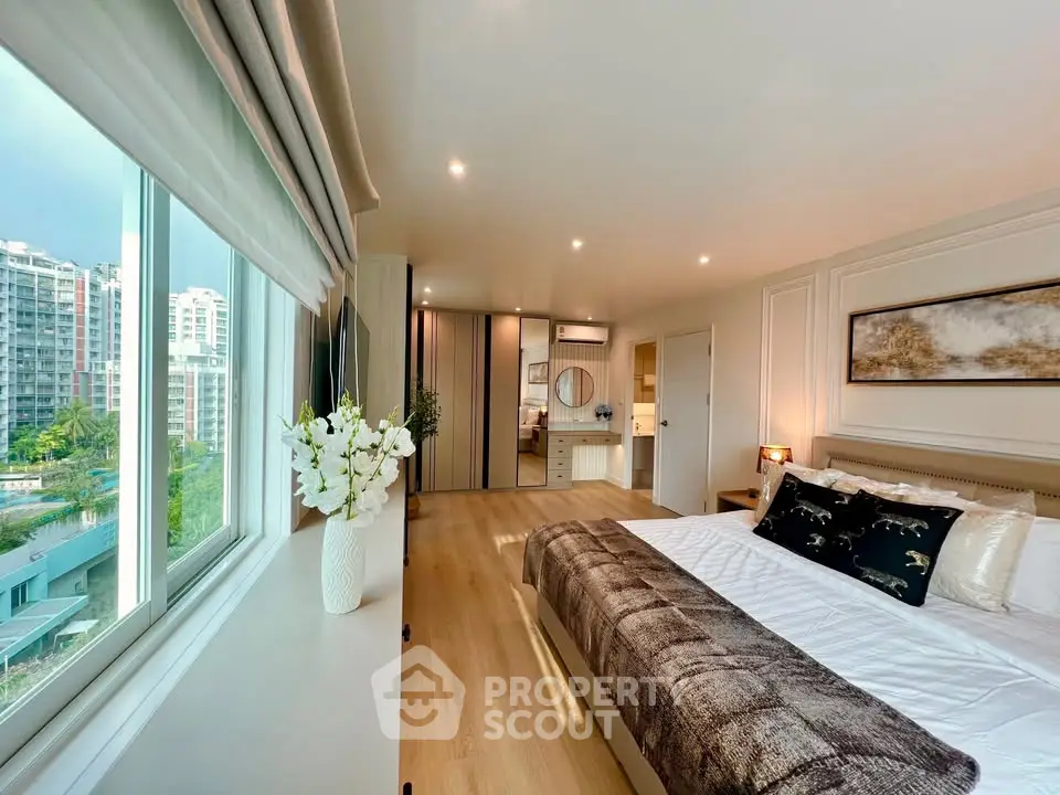 Luxurious bedroom with large window offering stunning city views, elegant decor, and ample natural light.