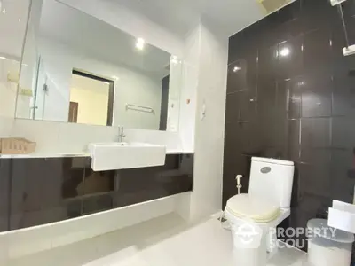 Sleek modern bathroom with glossy dark tiles, large mirror, and white sanitary fixtures, perfect for contemporary urban living.