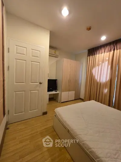 Cozy bedroom with wooden flooring, wardrobe, and natural light through curtains.