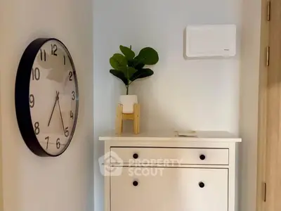 Stylish entryway with modern clock and potted plant on white cabinet
