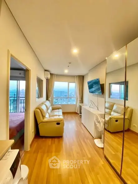 Modern living room with city view, featuring sleek furniture and large mirror for spacious feel.