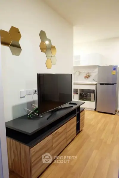 Modern living room with sleek TV stand and open kitchen layout featuring stainless steel appliances.
