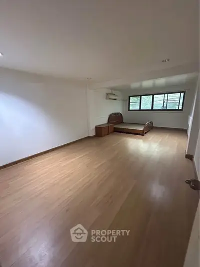 Spacious bedroom with wooden flooring and natural light
